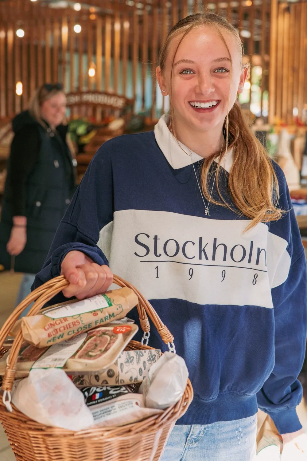 A smiling customer carrying a wicker basket of shopping in the Ginger Butchers farm shop in Matlock