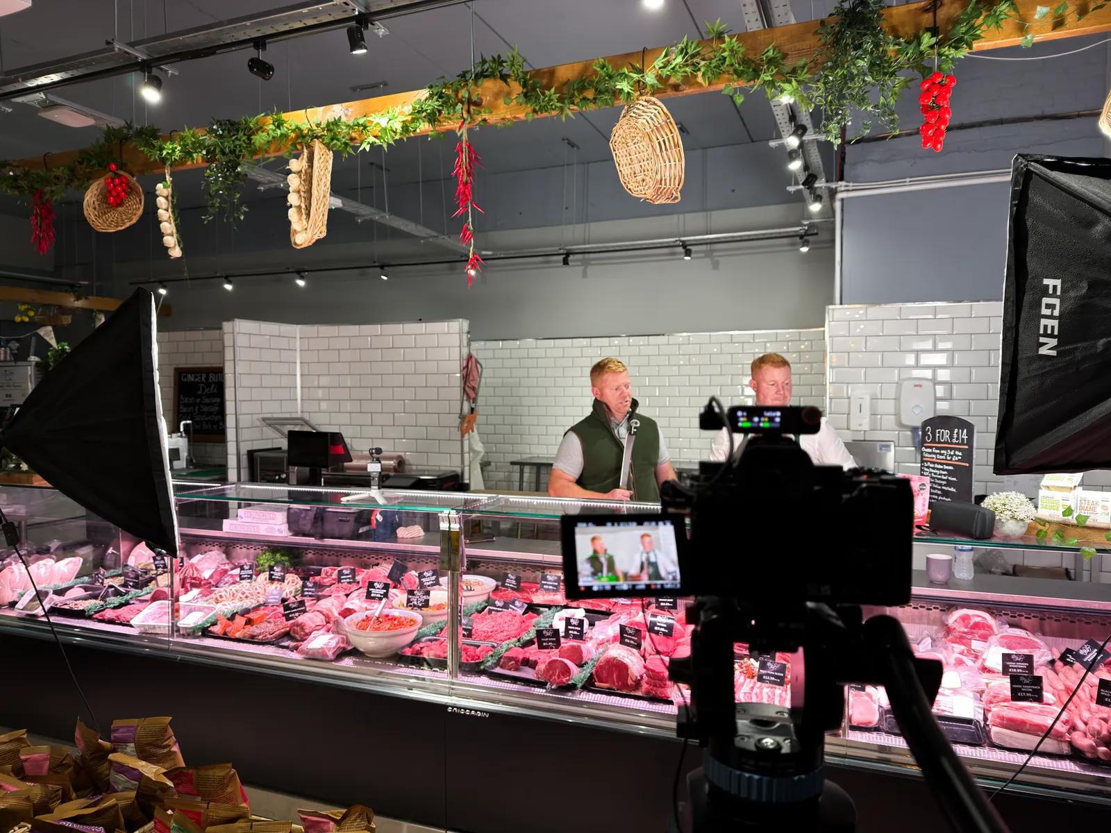 Camera on a tripod filming the butcher behind the counter at Ginger Butchers, with lights either side