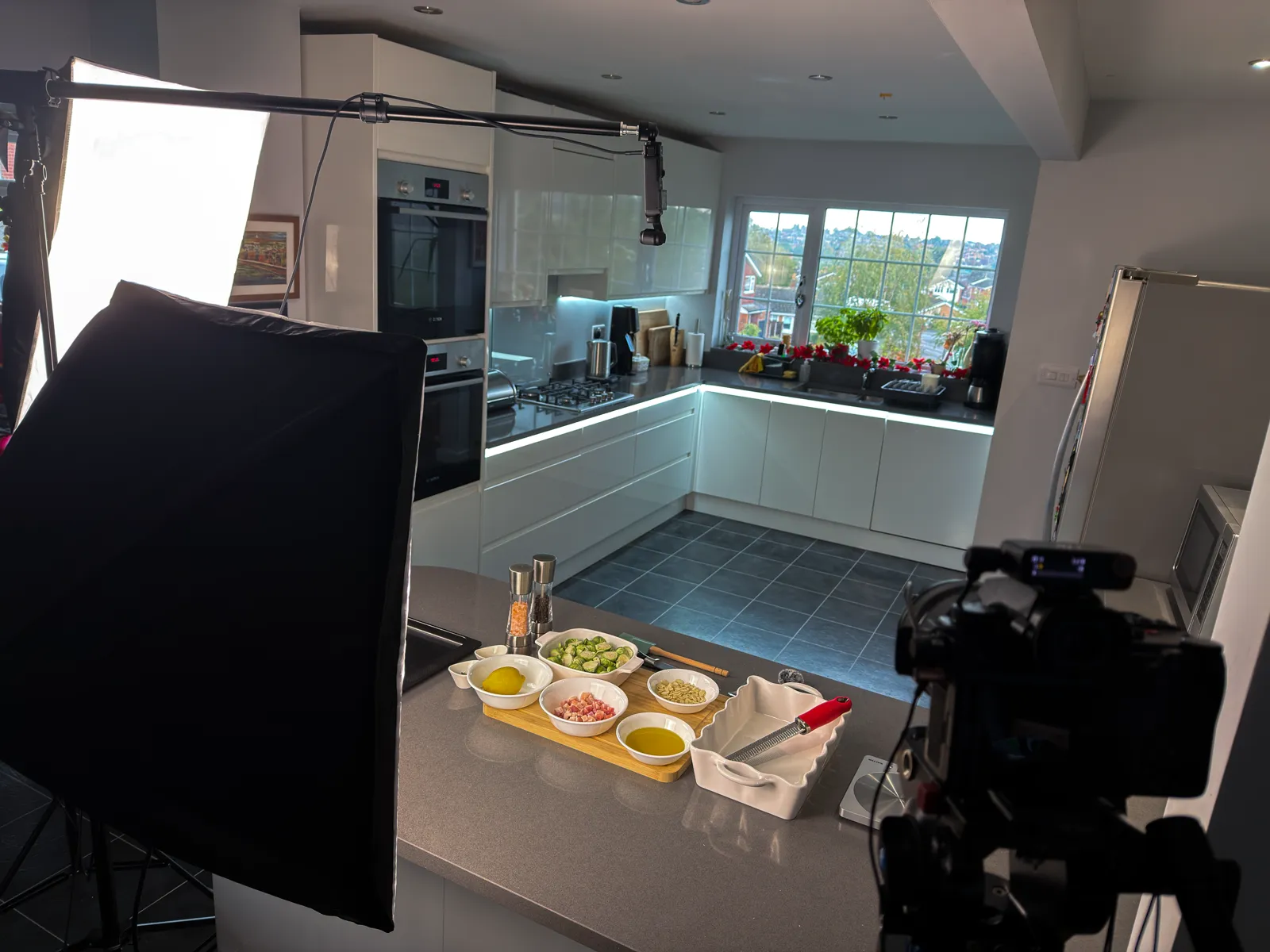 A camera and a softbox light set up in a modern kitchen, ready to film food being prepared on the worktop