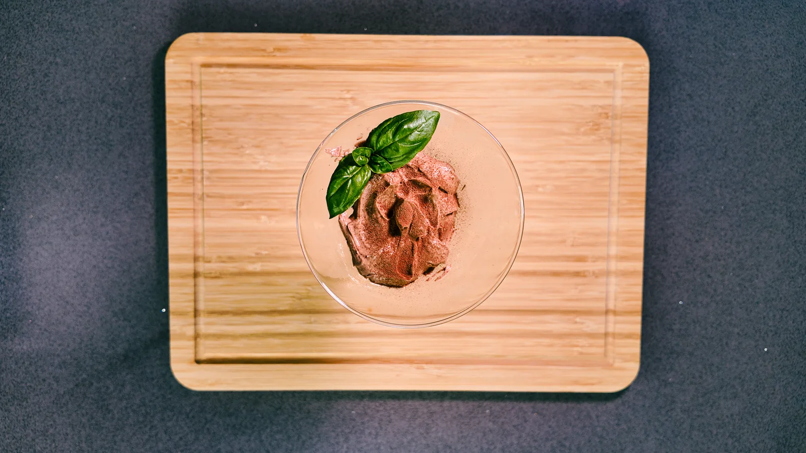 A chocolate keto cheesecake pot with basil on a wooden board, from above