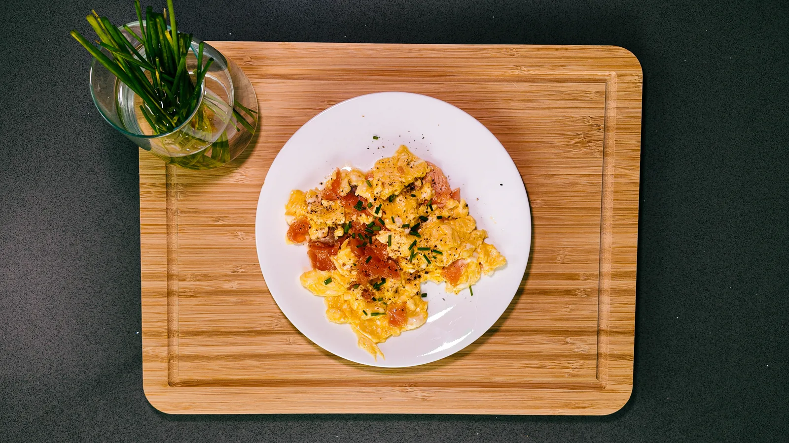 Scrambled eggs with smoked salmon and chives on a white plate on a wooden board, from above