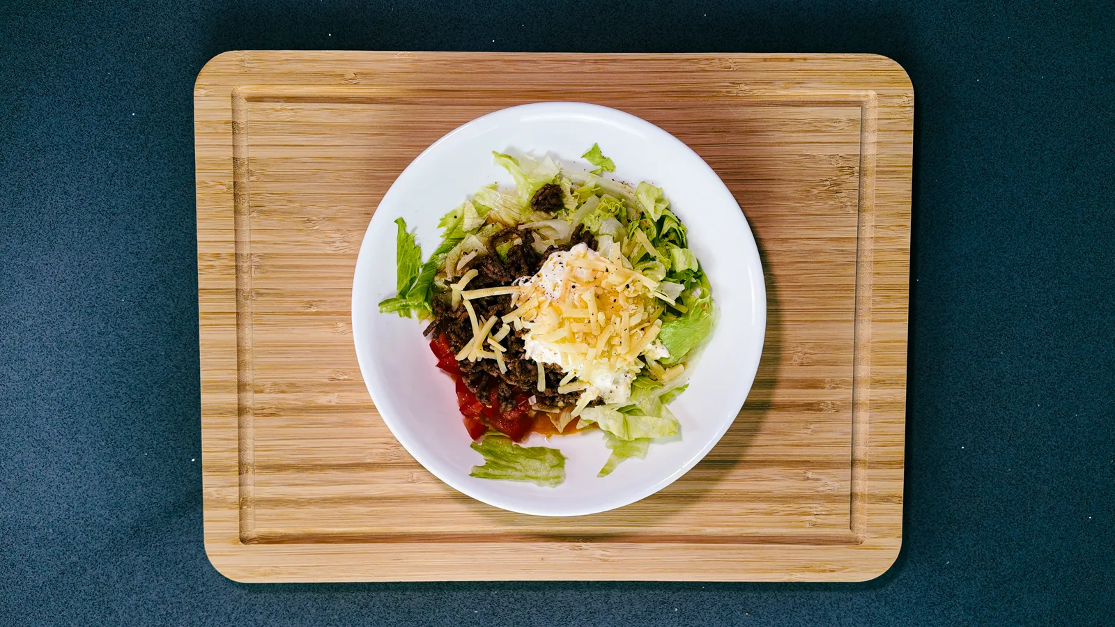 A cheesy beef taco bowl on a wooden board, shot from above