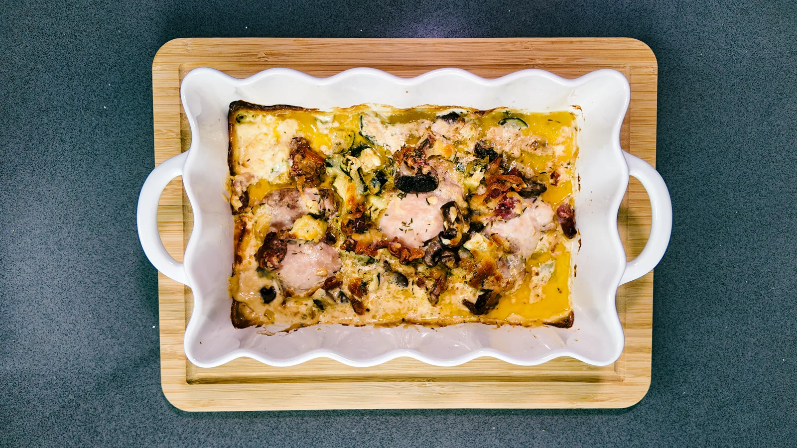 A creamy chicken and bacon traybake in a white dish on a wooden board, from above