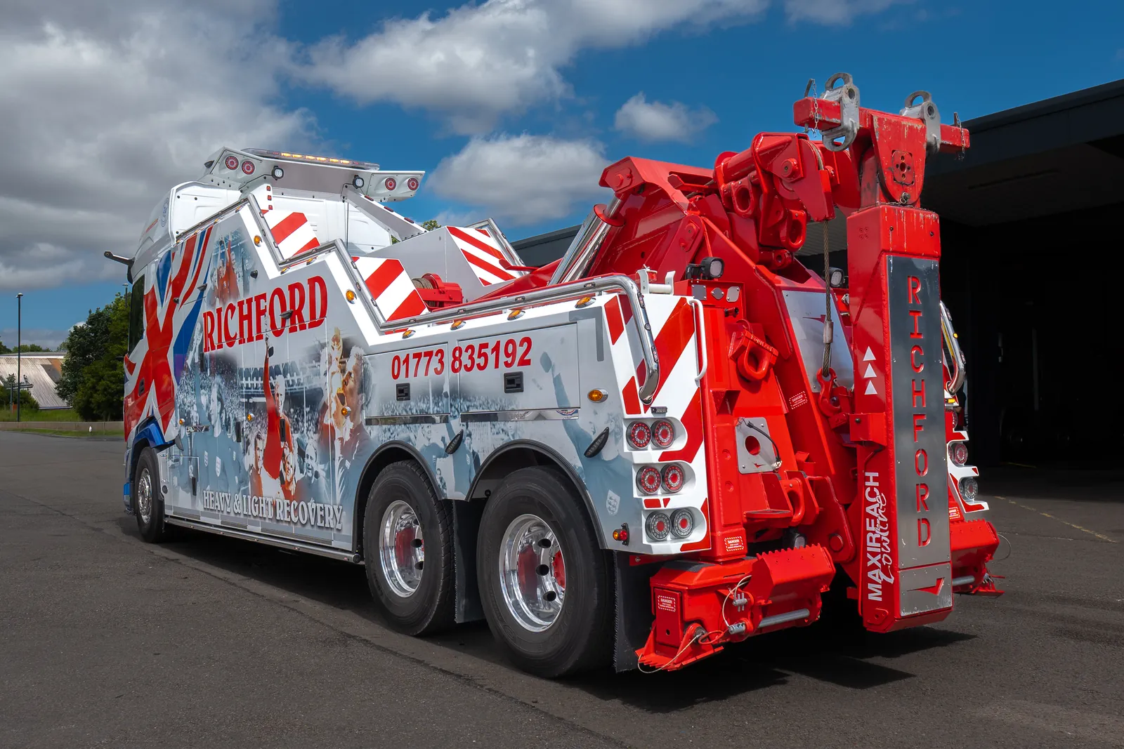 A rear three-quarter view of a red and white Richford heavy recovery truck with its boom and underlift, under a blue sky.